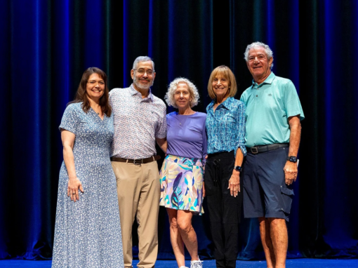 Five people stand in a line on a stage in front of a blue curtain.